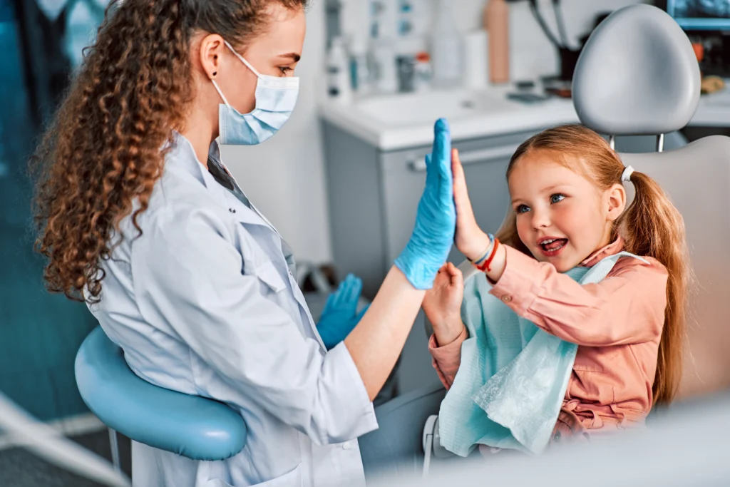 Fröhliches Mädchen beim Zahnarzt klatscht mit Zahnärztin ab – Symbol für eine positive Behandlungserfahrung dank Zahnzusatzversicherung für Kinder
