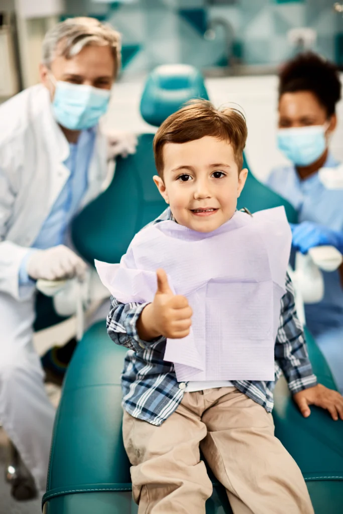 Glücklicher Junge beim Zahnarzt mit Daumen hoch – symbolisiert sorglose Zahngesundheit dank Zahnzusatzversicherung für Kinder