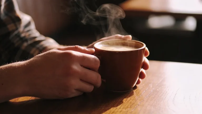 Hände halten dampfende Kaffeetasse auf Holztisch